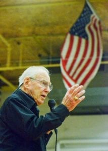 Retired NASA Astronaut Jim Lovell speaks passionately about his time in space, standing in front of an American flag in Bozeman High School gymnasium.