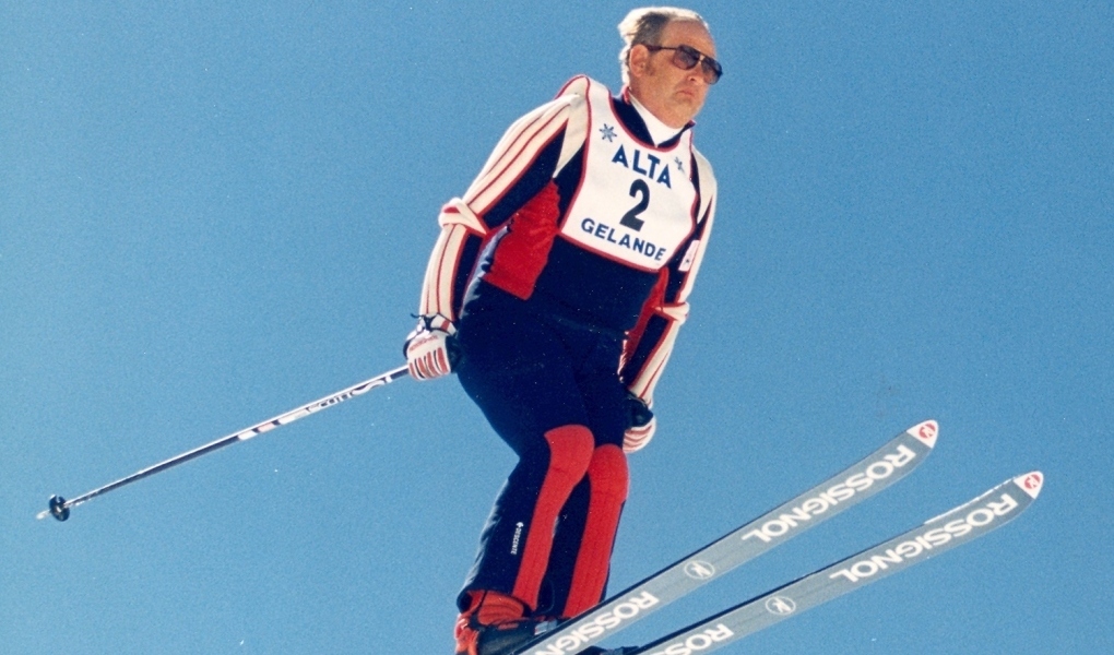 US Ski Hall of Fame athlete Alan Engen soars on a pair of skis, wearing red, white and blue snow suit and Alta bib.
