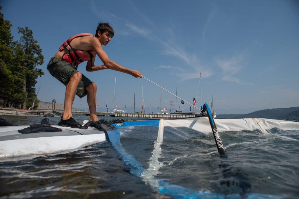 A Boy Scout pulls a windsurfing sail out of the water at summer camp, demonstrating independence and resilience.
