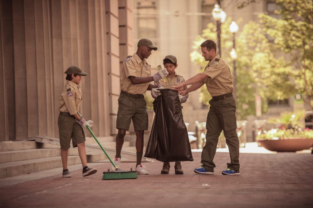 Three Scouts and a Scout Leader in uniform collect trash as community service in a large city.
