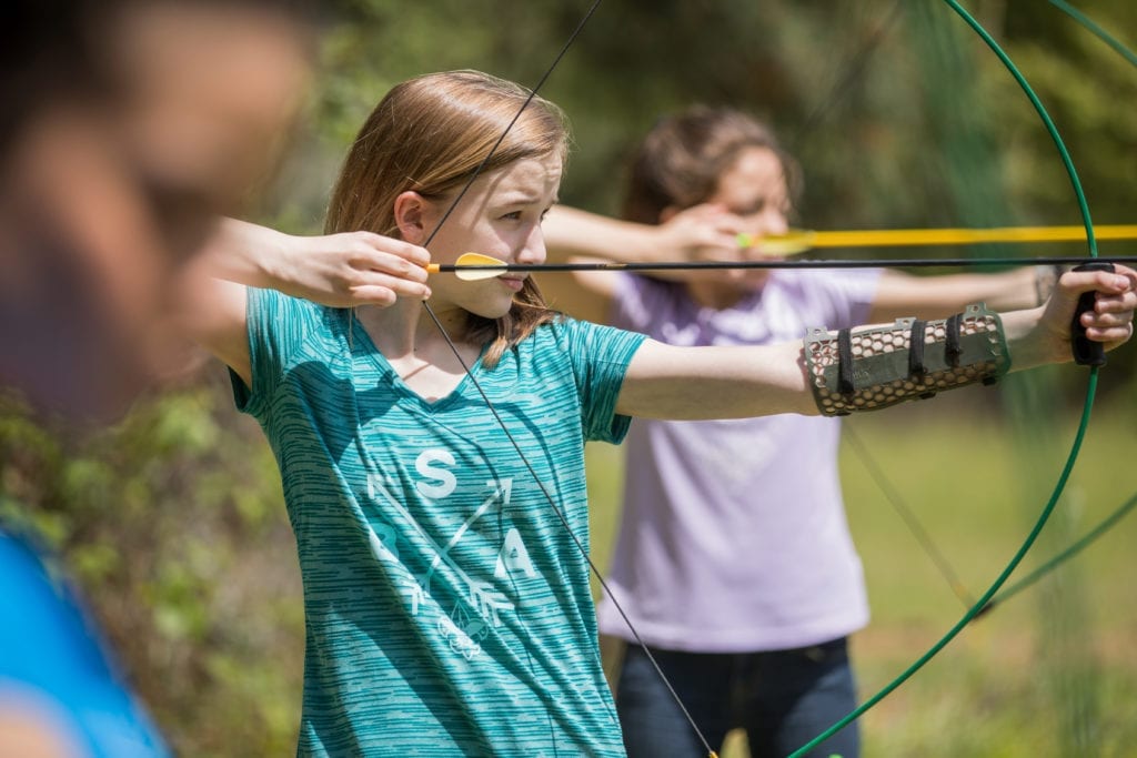 Two girls focus on targets while practicing archery at summer camp.