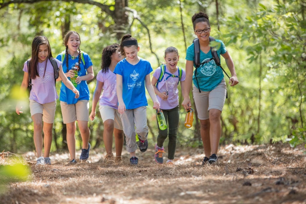 A group of girls participate in a Boy Scouts summer camp together, hiking in the wilderness.