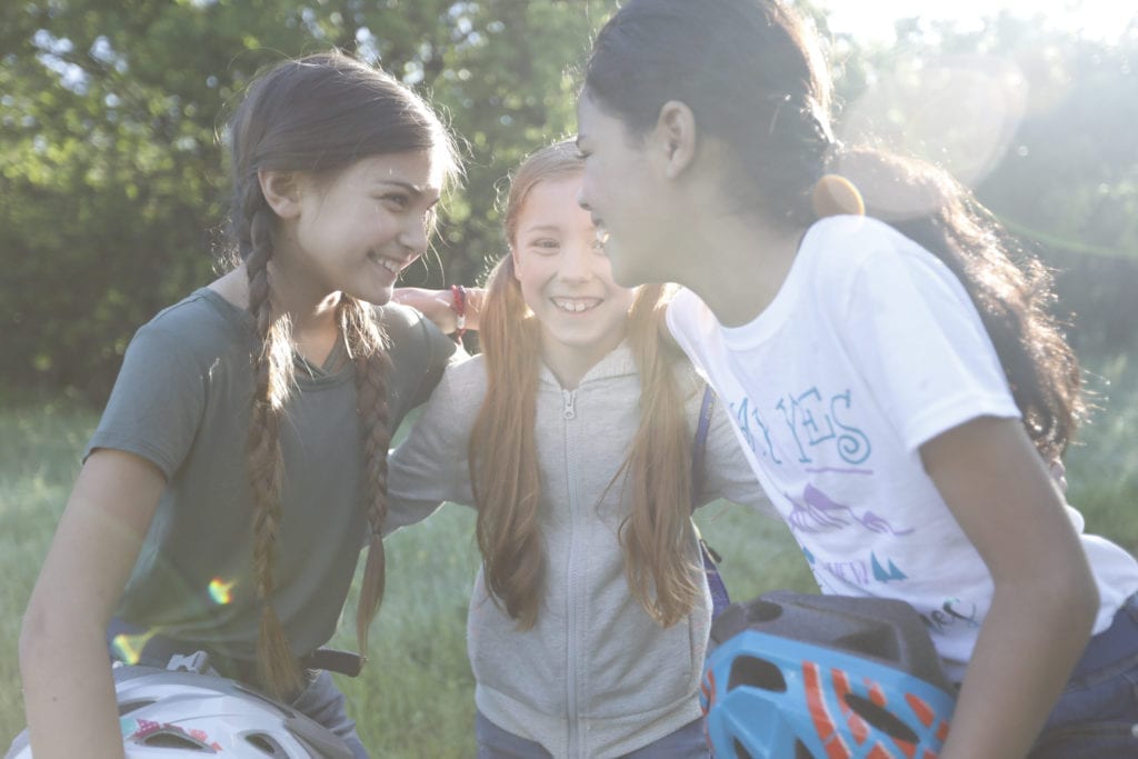Three girls talking in a huddle after biking outside.