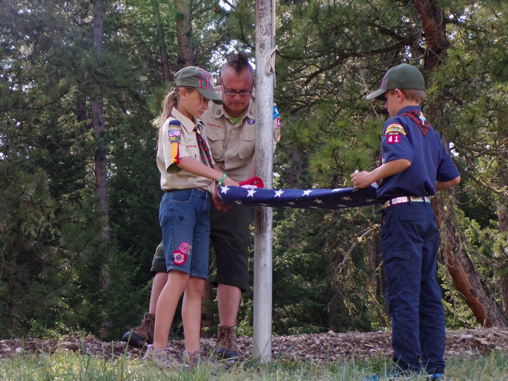 Two Scouts in uniform properly fold an American flag at summer camp.