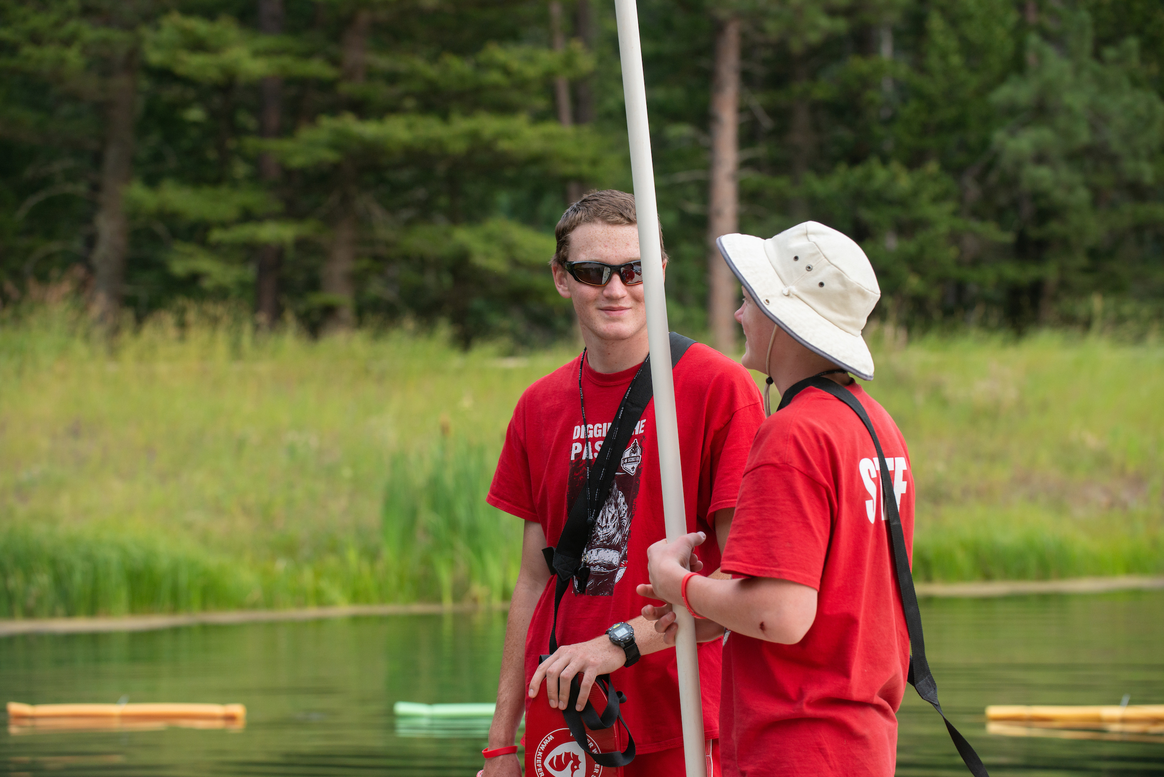 Two camp counselors in red t-shirts talk to each other on a dock
